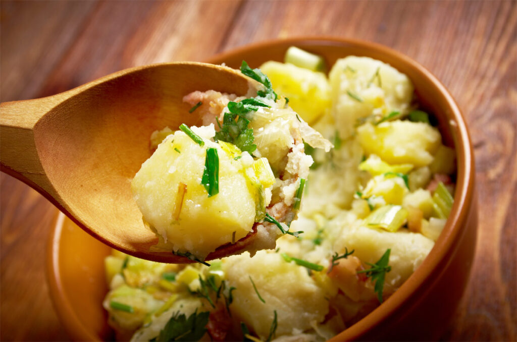 Kartoffelsalat in einer braunen Schüssel mit Holzlöffel als Beilage für Pulled Pork