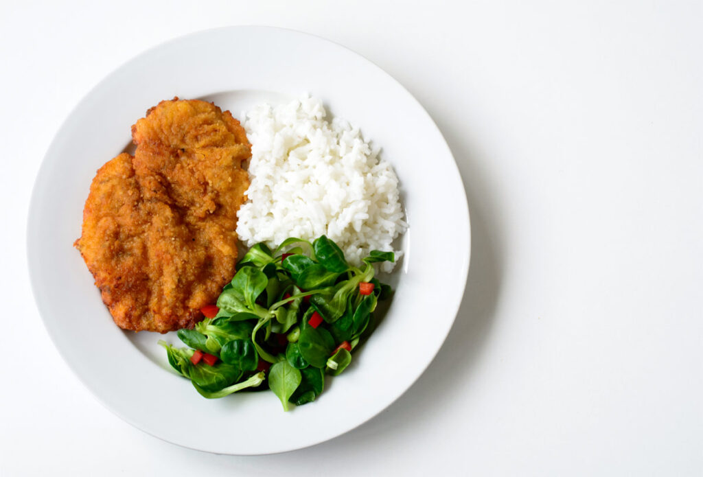 Schnitzel mit Reis und Salat auf einem Teller.