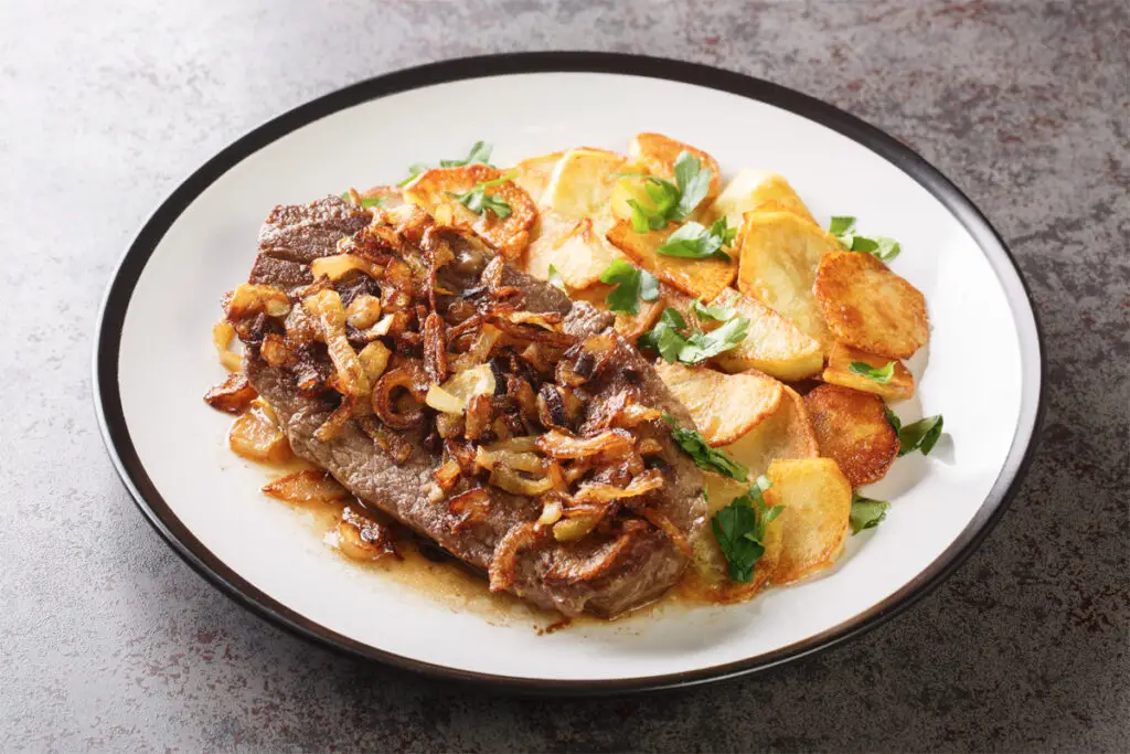 Steak mit Bratkartoffeln auf einem Teller mit dunklem Rand.
