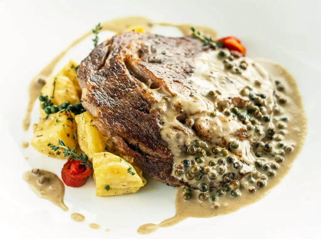 Rib Eye Steak mit cremiger Pfefferkornsauce auf einem weißen Teller.
