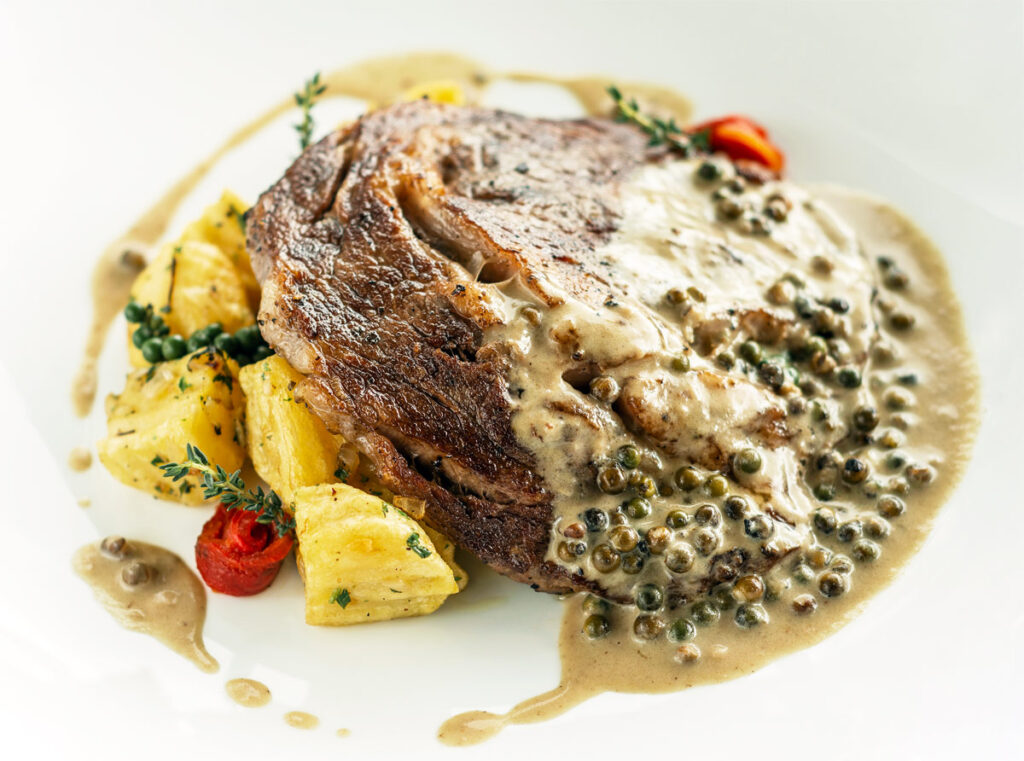 Rib Eye Steak mit cremiger Pfefferkornsauce auf einem weißen Teller.