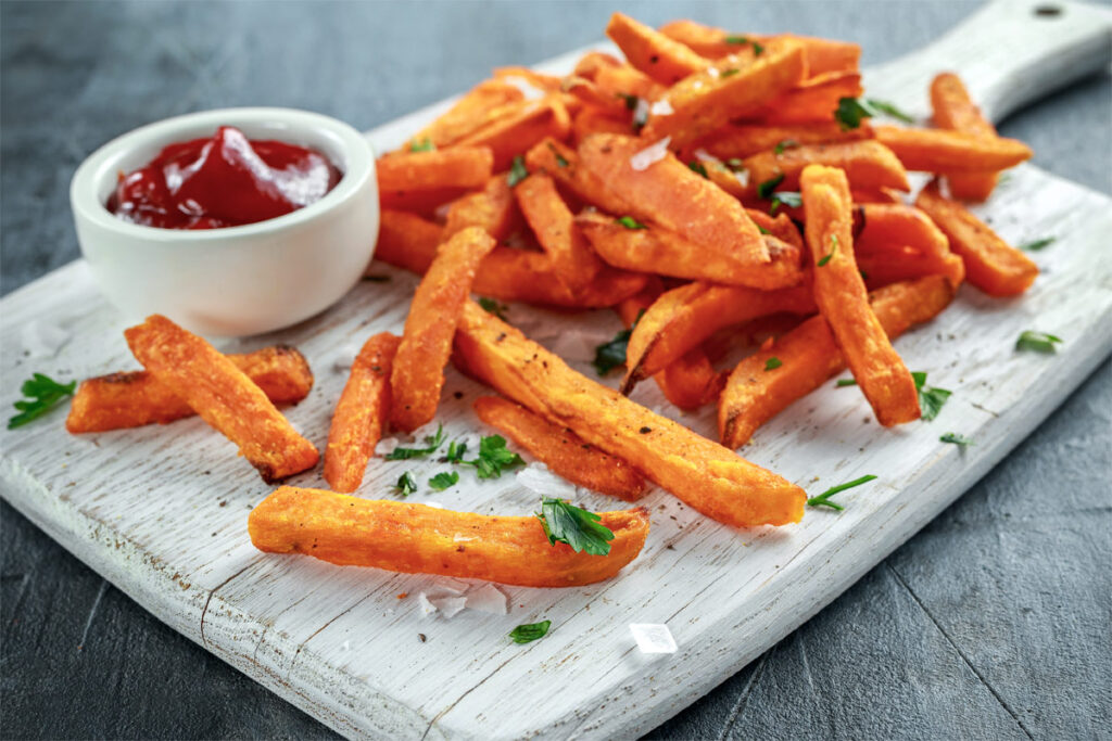 Süßkartoffelpommes auf einem Holzbrett mit Ketchup