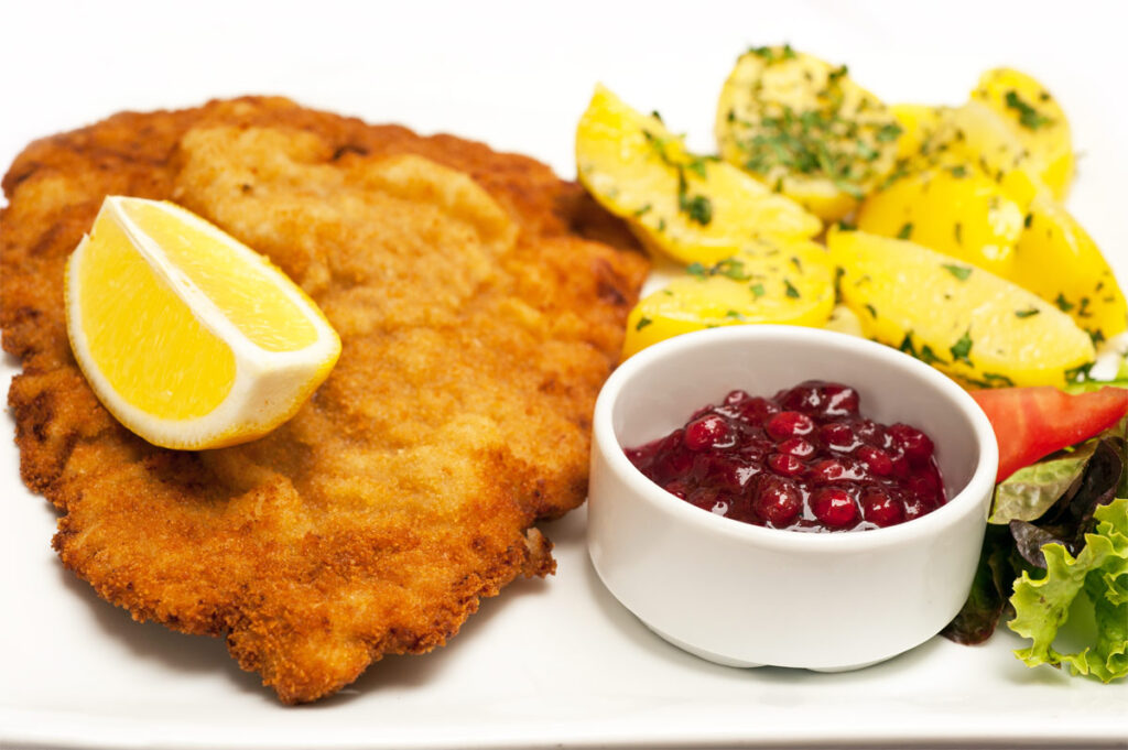 Wiener Schnitzel mit Preiselbeeren, Zitronenscheiben und Kartoffelsalat.