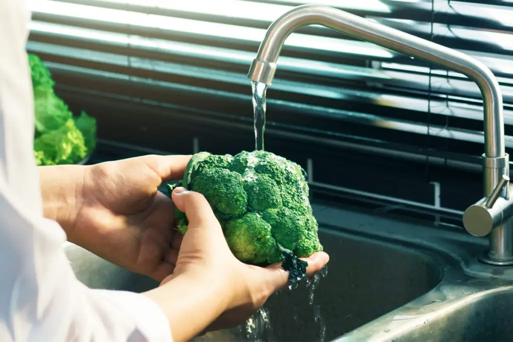 Frau wäscht Brokkoli unter fließendem Wasser