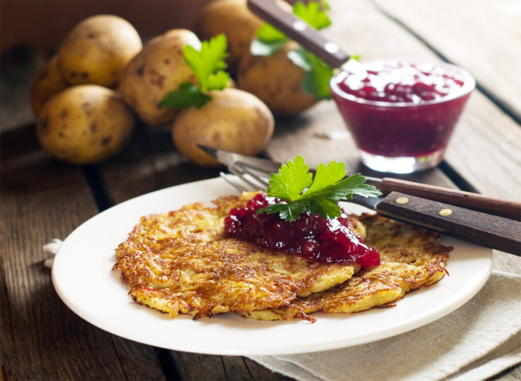 Zwei Kartoffelpuffer auf einem weißen Teller mit Preiselbeeren.