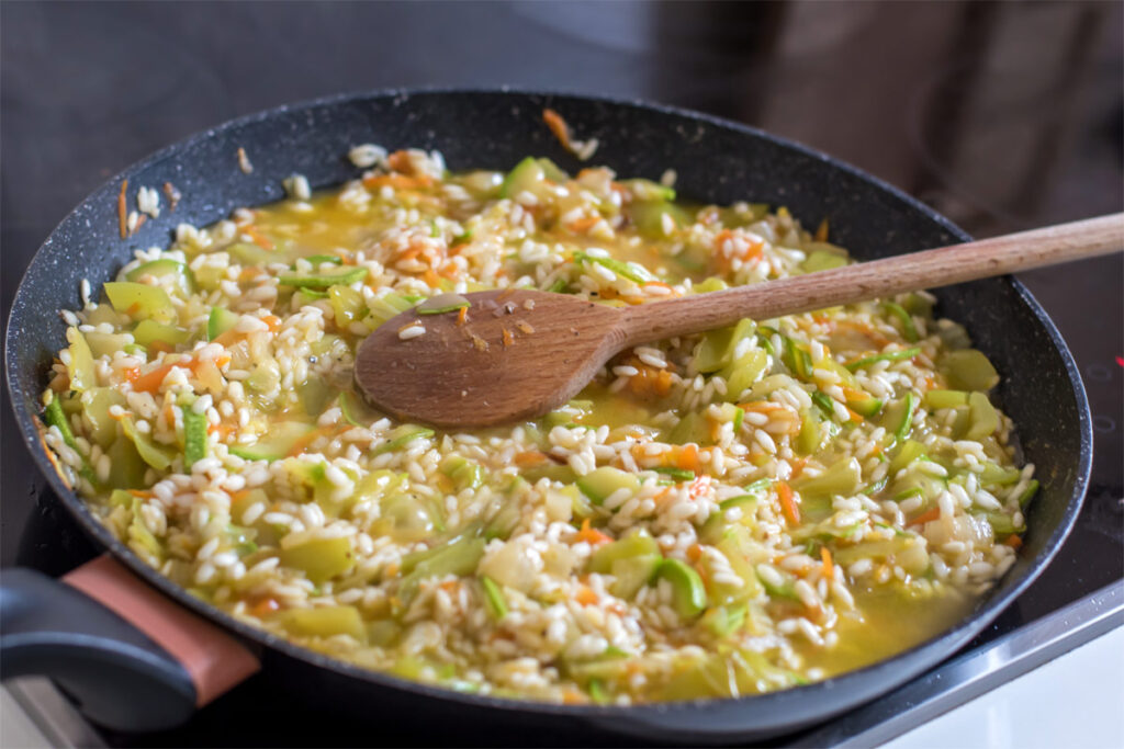 Risotto kochen in einer Pfanne mit Holzlöffel