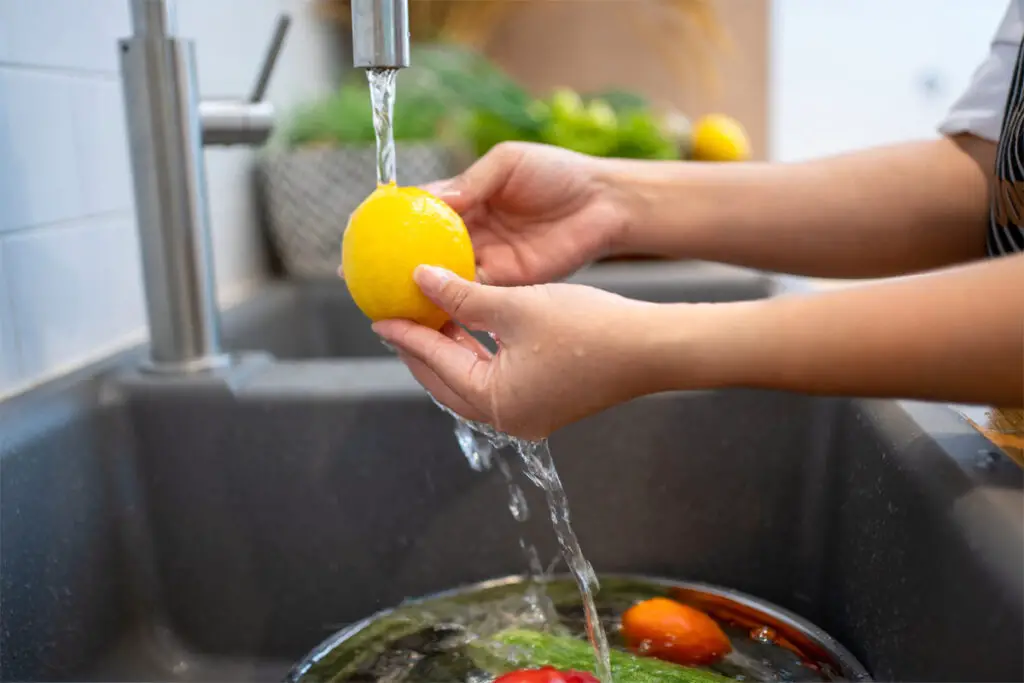 Frau wäscht eine Zitrone im Waschbecken unter dem Wasserhahn