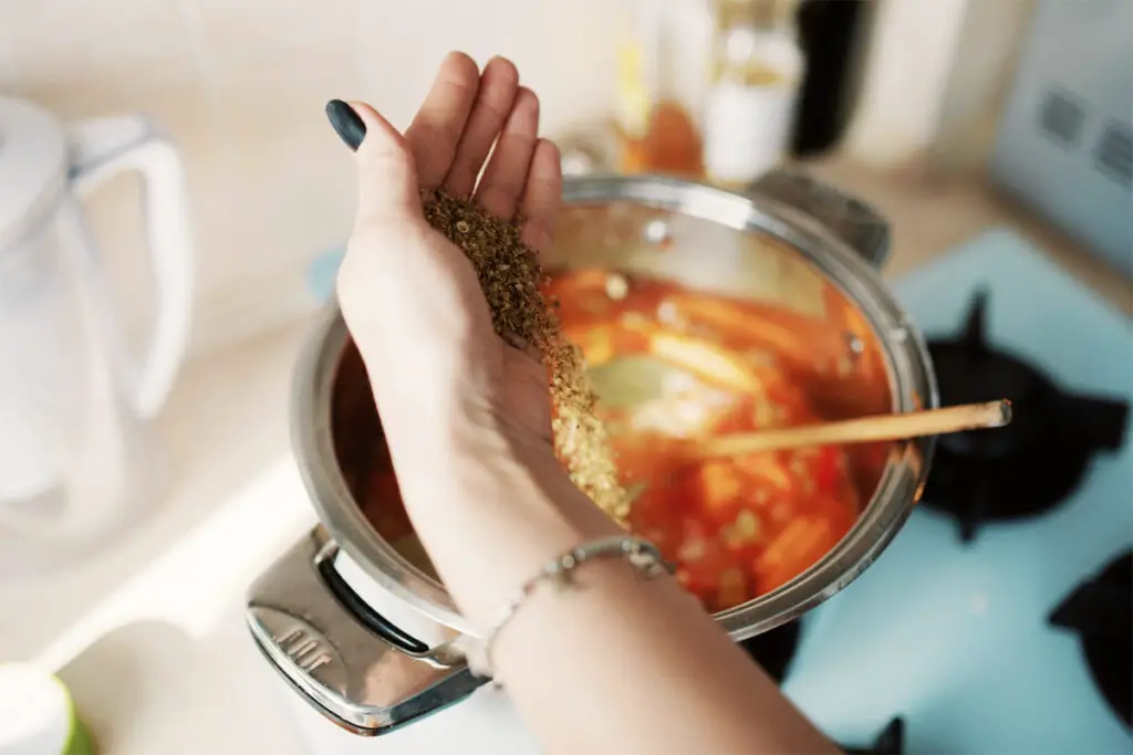 Frau gibt frische Zutaten in die Kürbissuppe beim Kochen