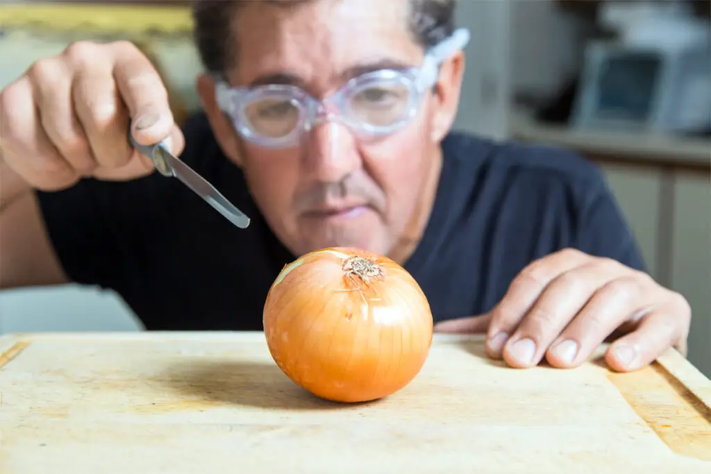 Mann mit Schutzbrille beim Zwiebeln schneiden