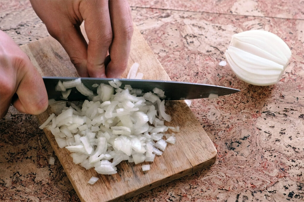 Zwiebelwürfel in verschiedenen Größen auf einem Holzbrett