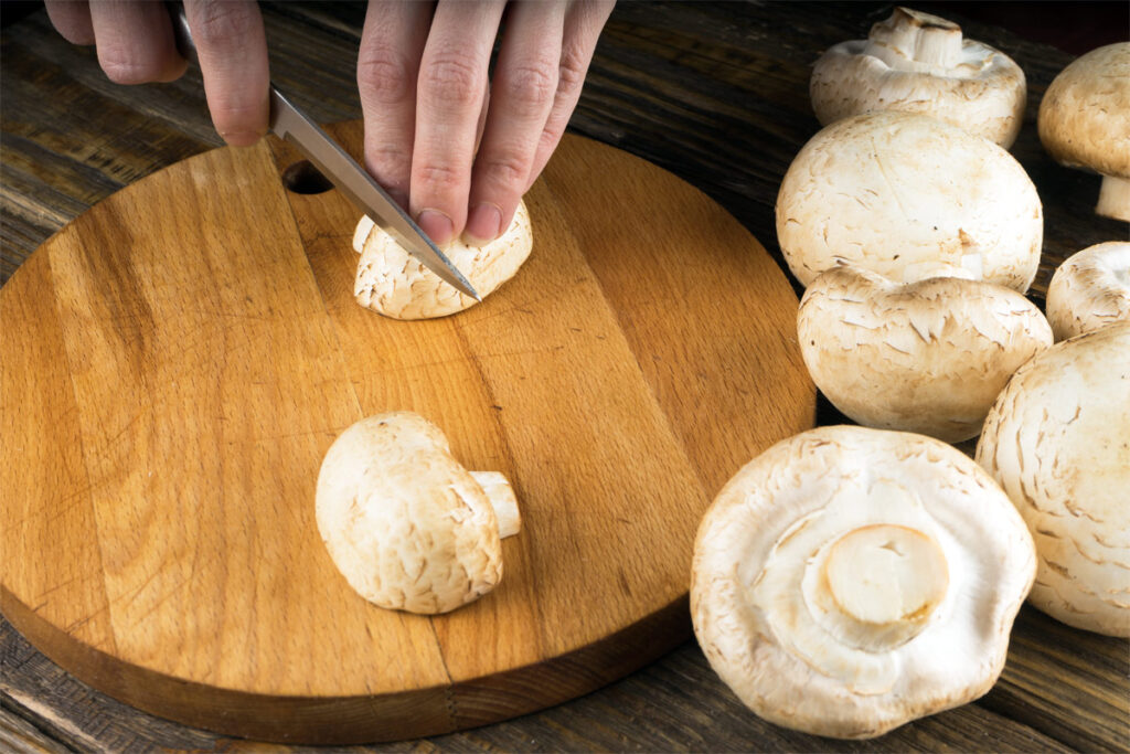 Frau schneidet Champignons auf einem Holzbrett mit einem Messer