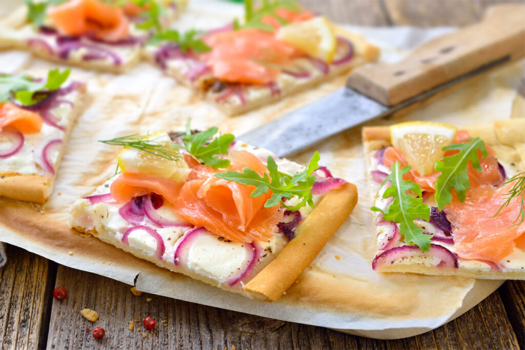 Flammkuchen mit Räucherlachs aufgeschnitten auf einem Holzbrett