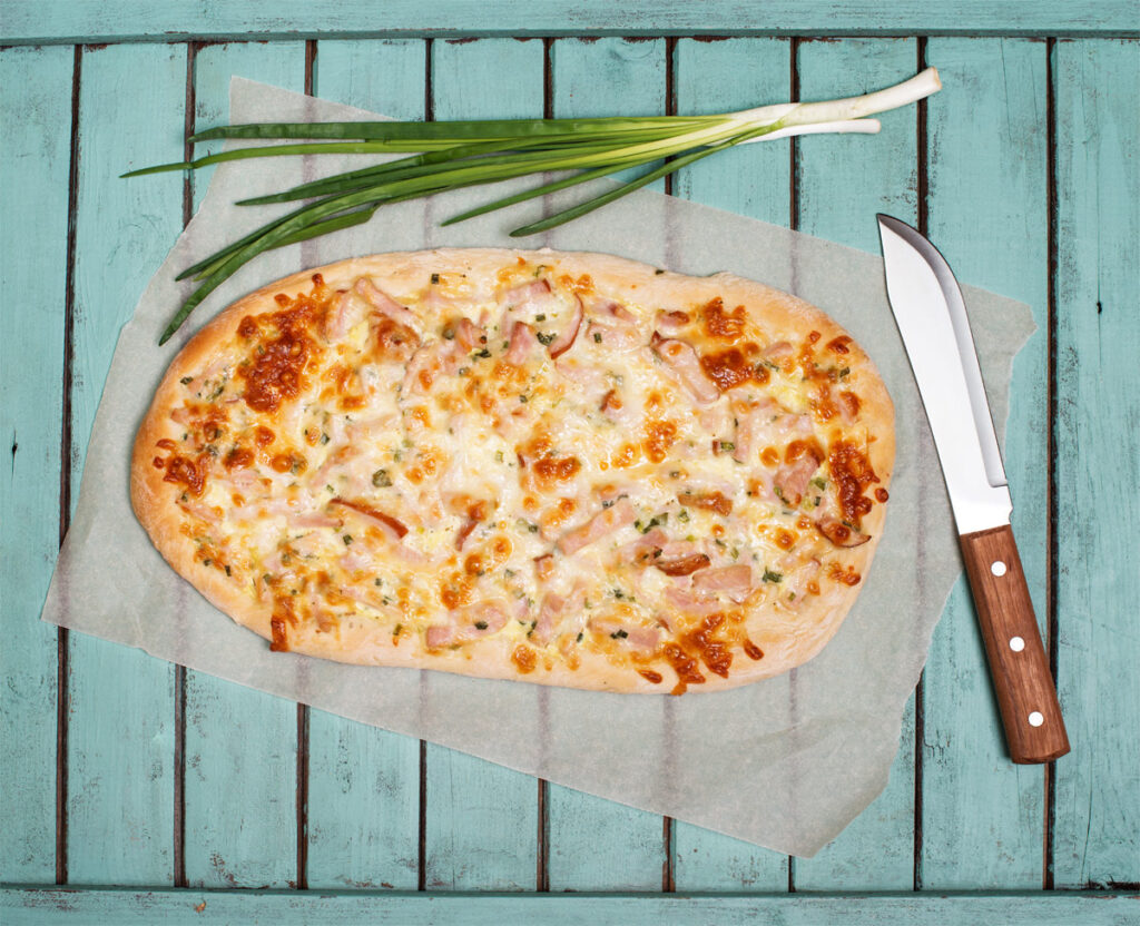 Flammkuchen glutenfrei auf einem Holztisch mit Messer und Lauchzwiebeln