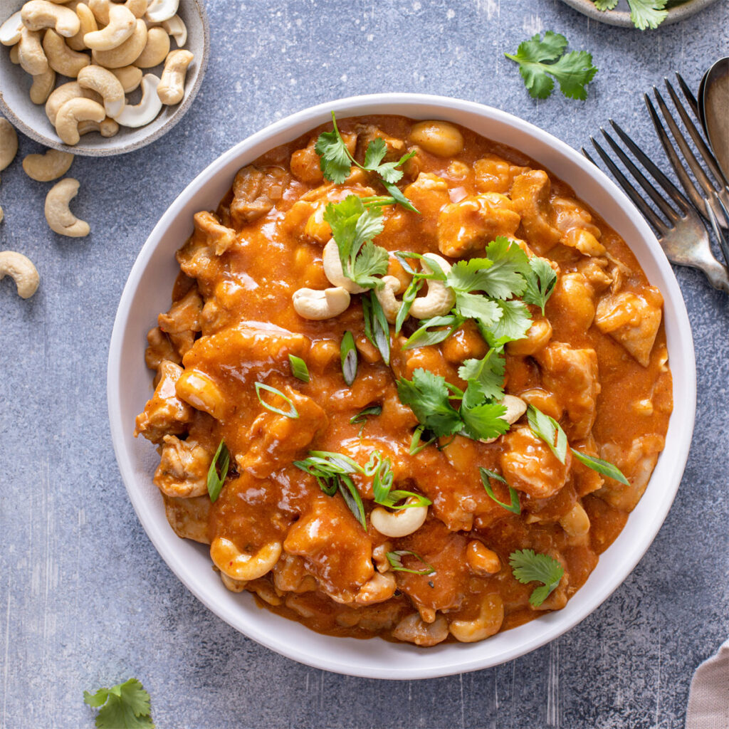 Weiße Schüssel mit thailändischen Hähnchencurry mit Cashewnüssen und Kräutern