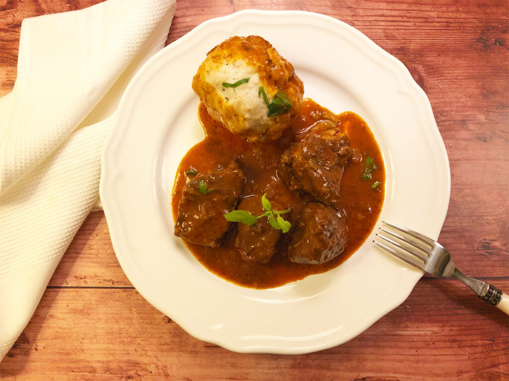 Hirschgulasch mit Semmelknödel auf einem weißen Teller