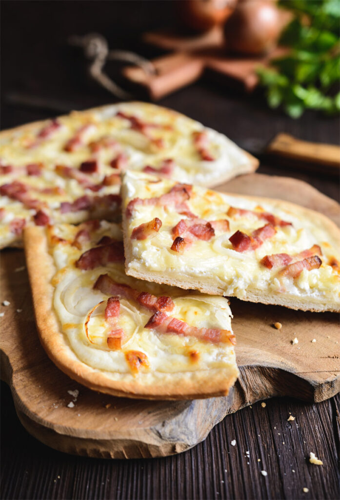 In Stücken aufgeschnittener Flammkuchen auf einem Holzbrett.